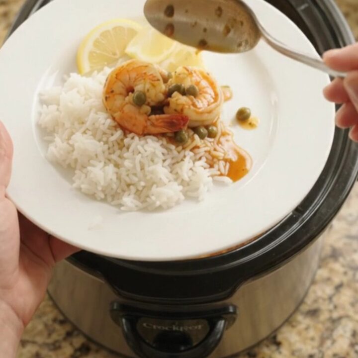Crockpot full of jumbo shrimp in a bubbling crimson Cajun butter sauce with lemon slices and capers