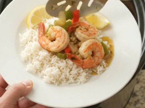 A slow cooker filled with jumbo shrimp, bell peppers, and onions in a golden garlic butter sauce, garnished with parsley.