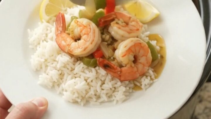 A slow cooker filled with jumbo shrimp, bell peppers, and onions in a golden garlic butter sauce, garnished with parsley.