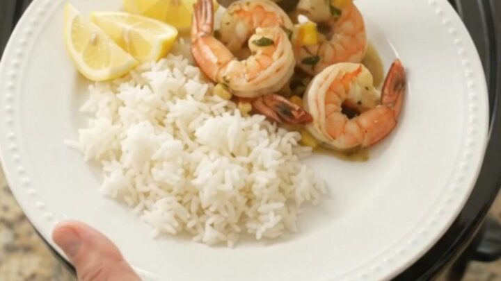 Slow cooker full of jumbo shrimp, corn, and garlic in a golden butter sauce with steam rising.