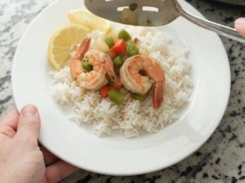 Slow-cooker herb butter shrimp with bell peppers and onions in a golden sauce, served over white rice with lemon wedges.