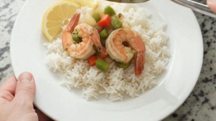 Slow-cooker herb butter shrimp with bell peppers and onions in a golden sauce, served over white rice with lemon wedges.