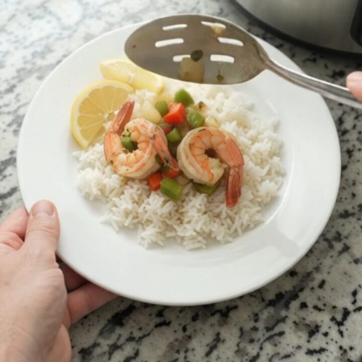 Slow-cooker herb butter shrimp with bell peppers and onions in a golden sauce, served over white rice with lemon wedges.