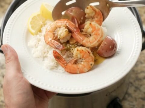 Slow cooker full of snow crab, shrimp, corn, and potatoes in golden butter sauce.