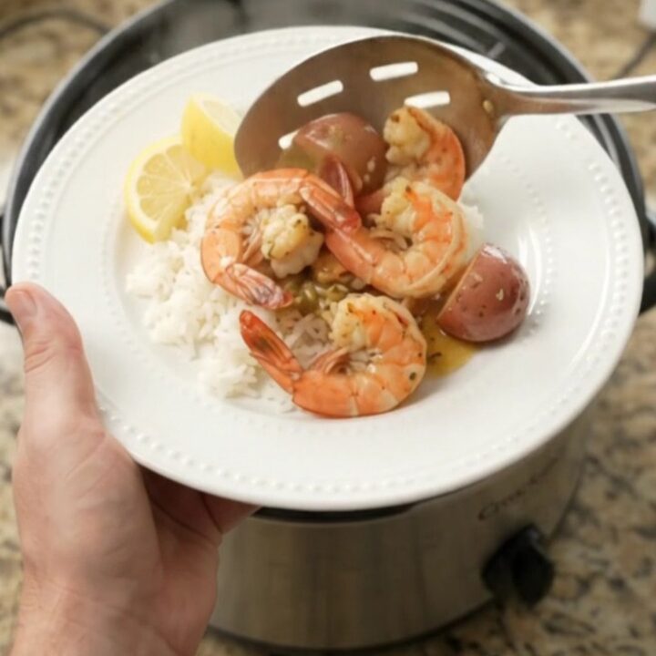 Slow cooker full of snow crab, shrimp, corn, and potatoes in golden butter sauce.
