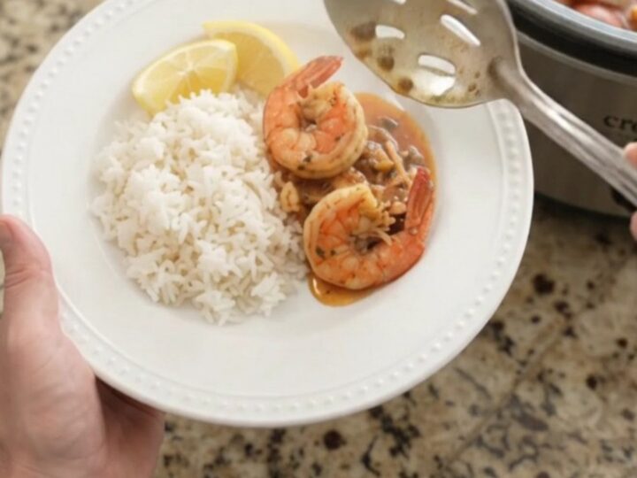 Slow cooker filled with snow crab, shrimp, corn, and potatoes in a red butter sauce