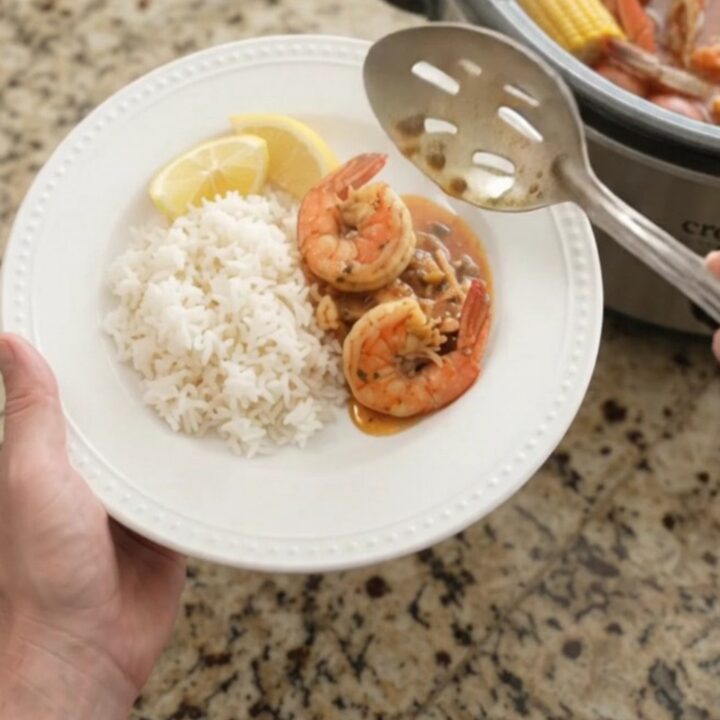 Slow cooker filled with snow crab, shrimp, corn, and potatoes in a red butter sauce