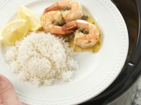 Slow cooker filled with snow crab clusters and shrimp in a golden butter sauce with lemon slices and capers.