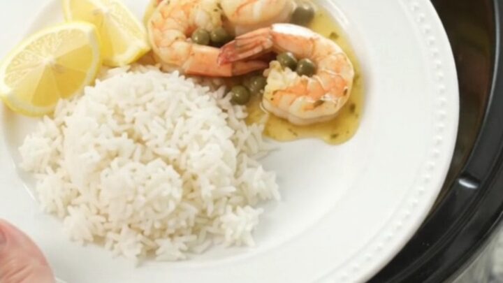 Slow cooker filled with snow crab clusters and shrimp in a golden butter sauce with lemon slices and capers.