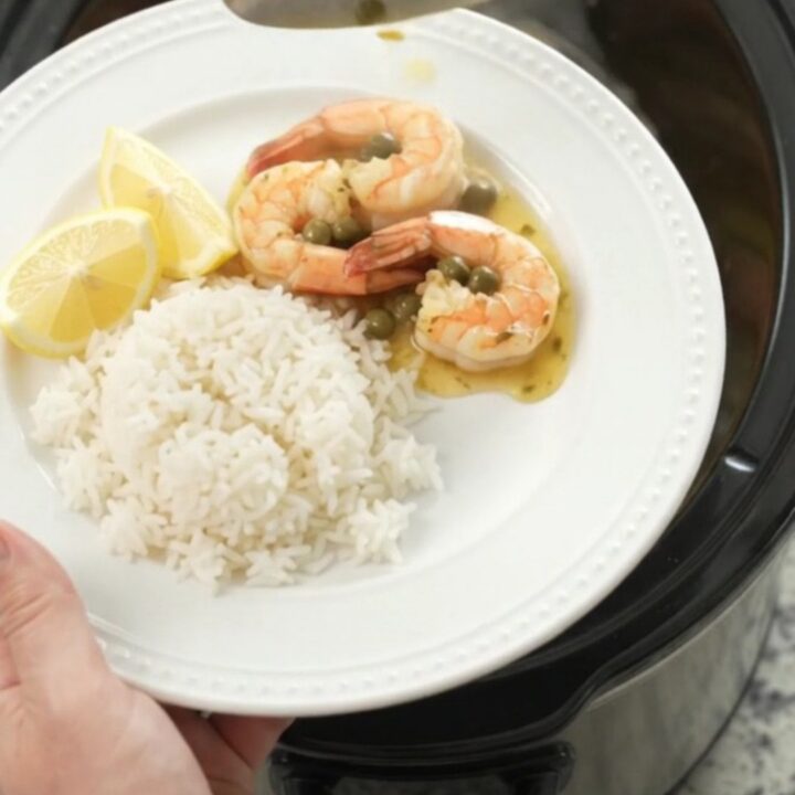 Slow cooker filled with snow crab clusters and shrimp in a golden butter sauce with lemon slices and capers.