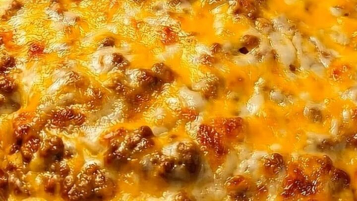 A metal spatula lifting a steaming, cheesy portion of cheeseburger casserole from a glass baking dish