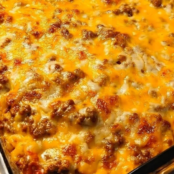 A metal spatula lifting a steaming, cheesy portion of cheeseburger casserole from a glass baking dish