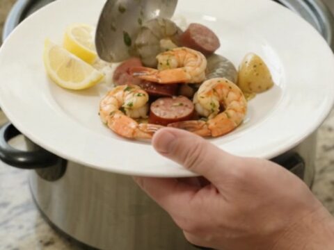 Slow cooker filled with snow crab, shrimp, and sausage in a buttery sauce