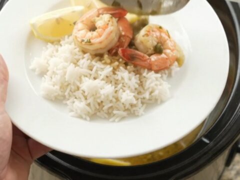 Slow cooker filled with snow crab clusters and shrimp in a golden butter sauce with lemon slices and capers.