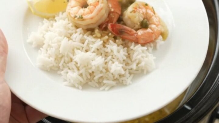 Slow cooker filled with snow crab clusters and shrimp in a golden butter sauce with lemon slices and capers.