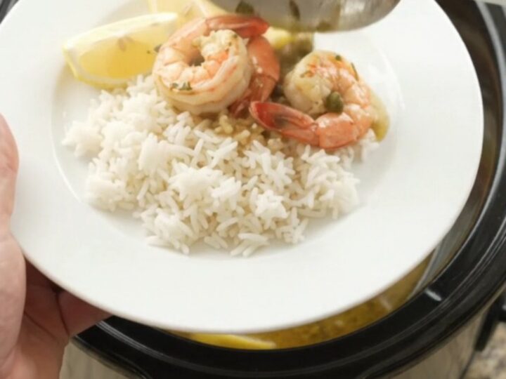 Slow cooker filled with snow crab clusters and shrimp in a golden butter sauce with lemon slices and capers.