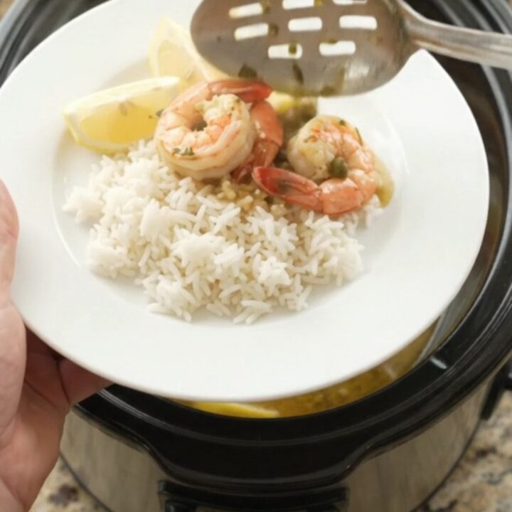 Slow cooker filled with snow crab clusters and shrimp in a golden butter sauce with lemon slices and capers.