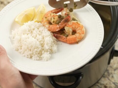 Slow cooker full of snow crab clusters and shrimp in a glossy chili-lime butter sauce with lemon slices and capers