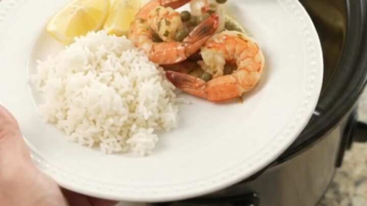 Slow cooker full of snow crab clusters and shrimp in a glossy chili-lime butter sauce with lemon slices and capers