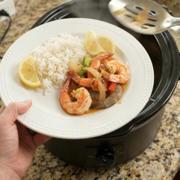 Snow crab clusters and shrimp in a slow cooker with red and green bell peppers and onions in a buttery sauce
