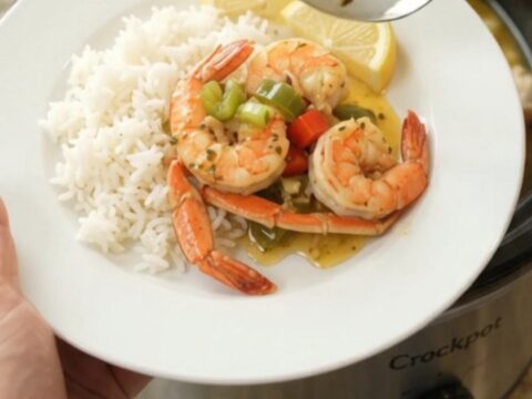 Slow cooker filled with snow crab clusters and shrimp in a garlic butter sauce with bell peppers and onions