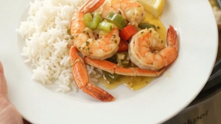 Slow cooker filled with snow crab clusters and shrimp in a garlic butter sauce with bell peppers and onions
