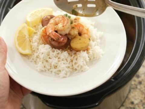 Slow cooker filled with lobster tails, shrimp, and Andouille sausage in a rich red butter sauce, topped with baby potatoes.