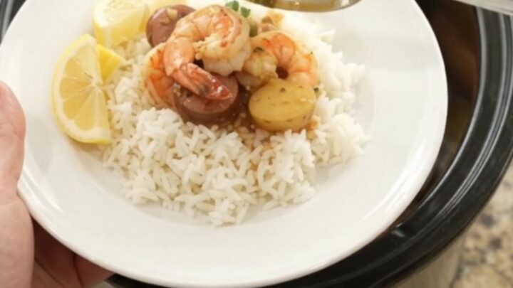 Slow cooker filled with lobster tails, shrimp, and Andouille sausage in a rich red butter sauce, topped with baby potatoes.