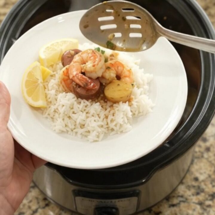 Slow cooker filled with lobster tails, shrimp, and Andouille sausage in a rich red butter sauce, topped with baby potatoes.
