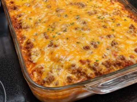 A steaming, cheesy Mexican casserole in a glass baking dish sitting on a black stovetop.