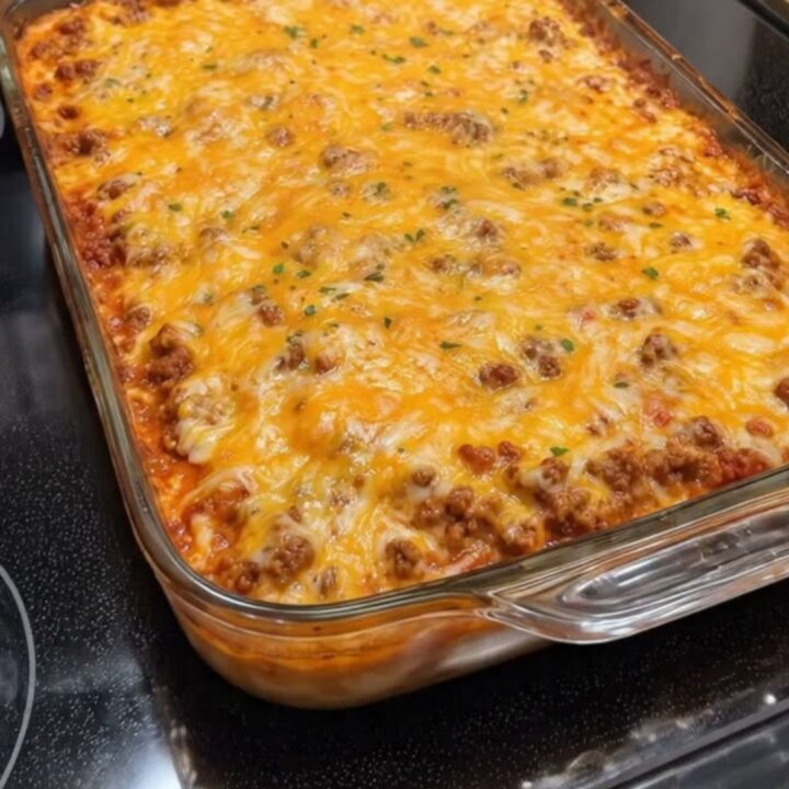 A steaming, cheesy Mexican casserole in a glass baking dish sitting on a black stovetop.