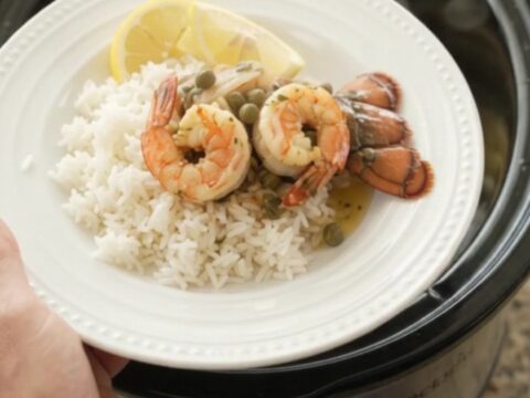 Slow cooker lobster tails and shrimp in a golden butter sauce with lemon slices and capers.