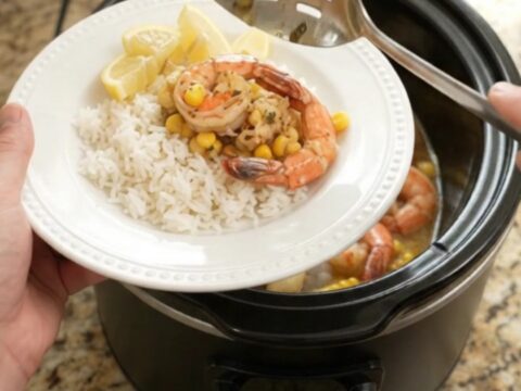 Slow cooker filled with lobster tails, shrimp, corn, and garlic in a golden butter sauce