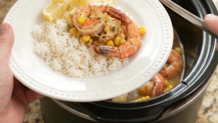 Slow cooker filled with lobster tails, shrimp, corn, and garlic in a golden butter sauce