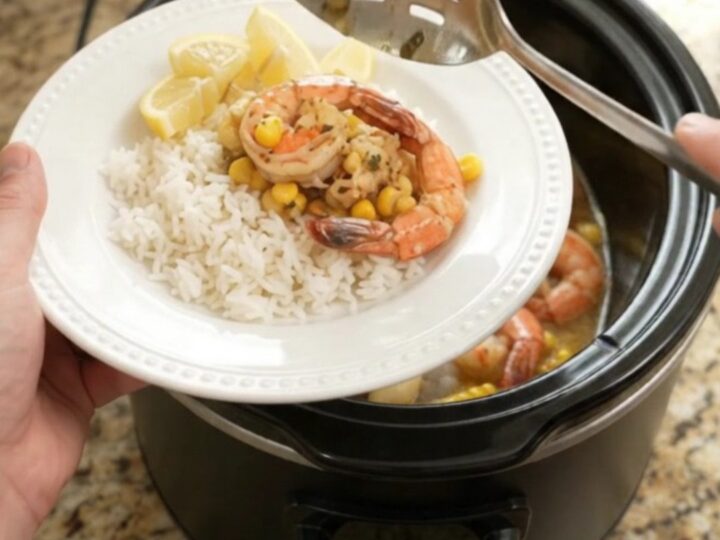 Slow cooker filled with lobster tails, shrimp, corn, and garlic in a golden butter sauce