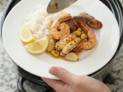 Crockpot with lobster tails, shrimp, corn, and garlic in a bubbling red butter sauce