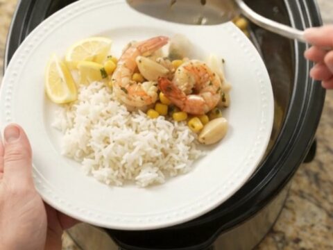 Slow cooker filled with buttered lobster tails, shrimp, corn, and garlic in a golden sauce