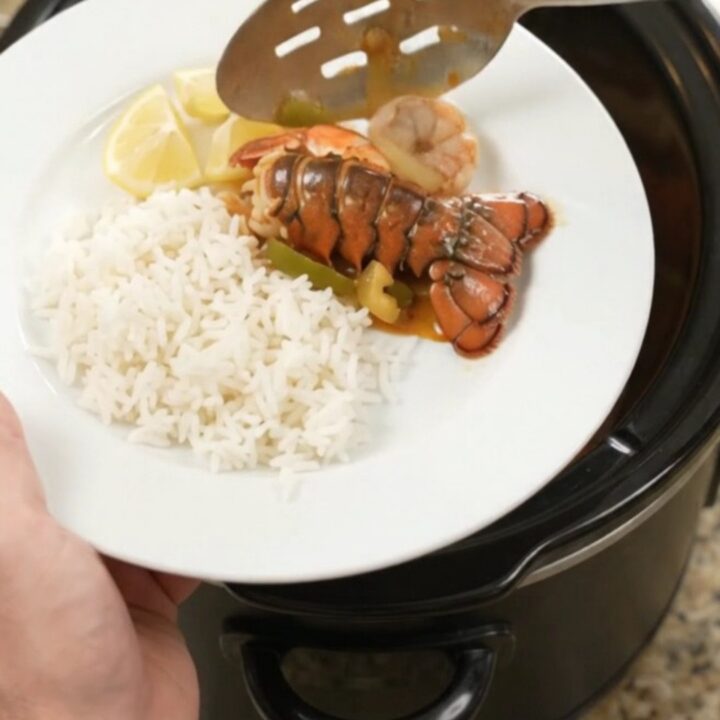Slow-cooker lobster tails and shrimp in spicy Cajun butter sauce with bell peppers and onions, served over rice.