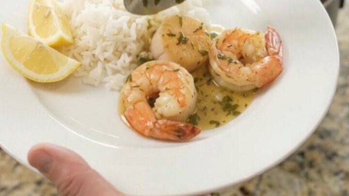 Slow cooker filled with golden sea scallops, shrimp, corn, and potatoes in a buttery herb sauce