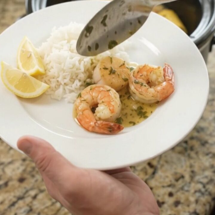 Slow cooker filled with golden sea scallops, shrimp, corn, and potatoes in a buttery herb sauce