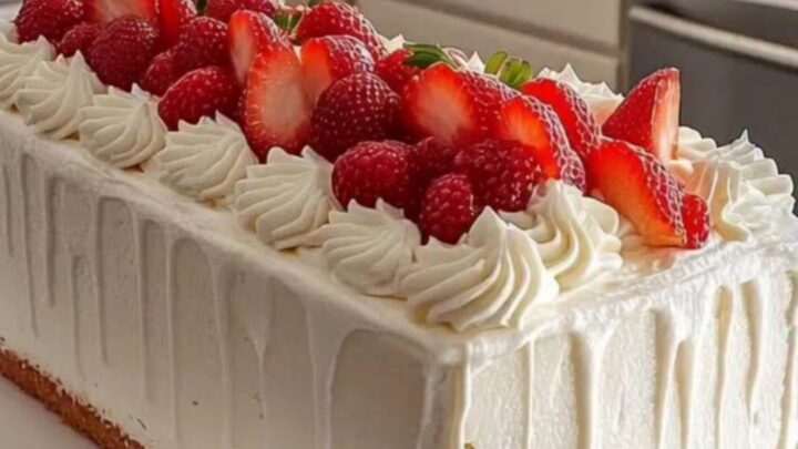 A beautiful rectangular strawberry cream cake with piped rosettes and fresh strawberry slices on a white platter.