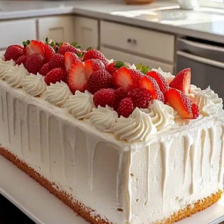 A beautiful rectangular strawberry cream cake with piped rosettes and fresh strawberry slices on a white platter.