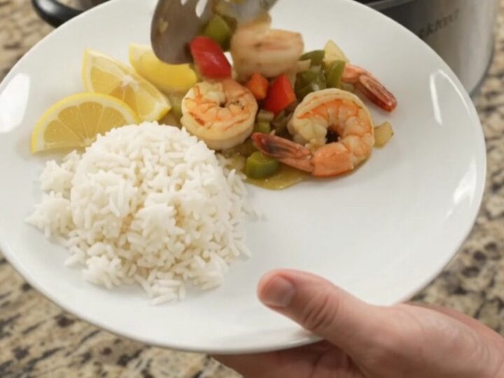 Slow cooker with golden scallops and shrimp in garlic butter sauce with bell peppers and onions.
