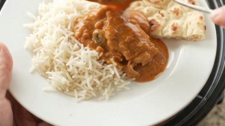 Slow cooker makhani chicken thighs in creamy tomato sauce, garnished with cream swirl, served over rice