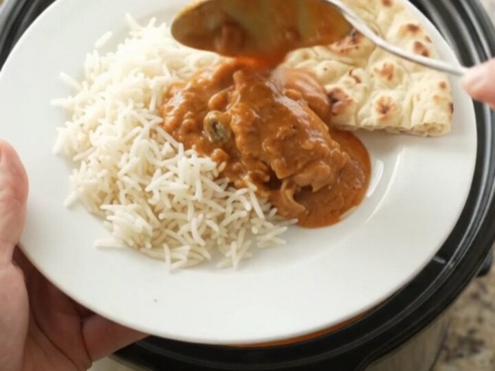 Slow cooker makhani chicken thighs in creamy tomato sauce, garnished with cream swirl, served over rice