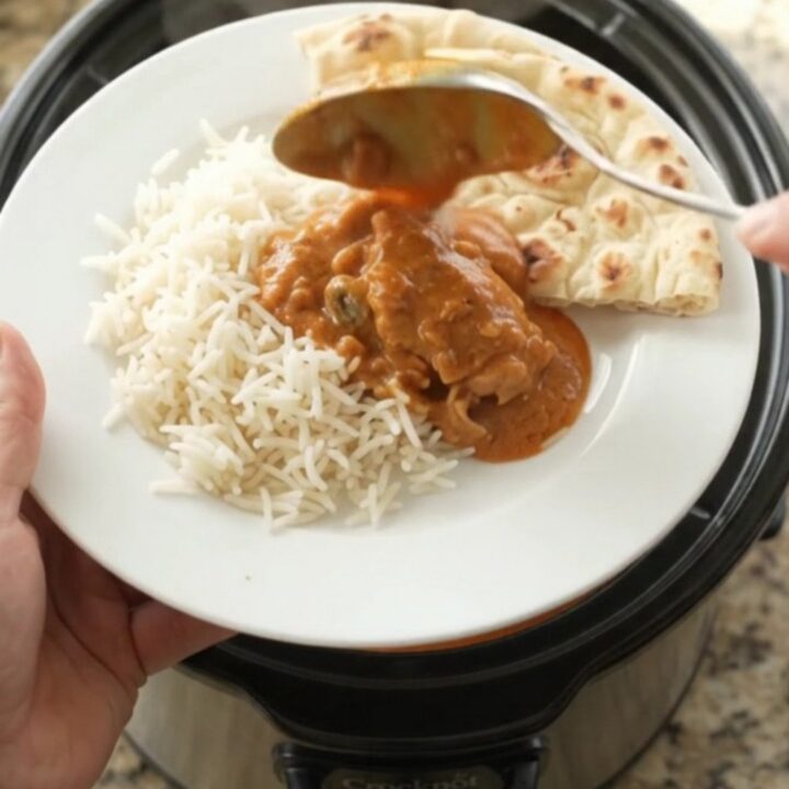 Slow cooker makhani chicken thighs in creamy tomato sauce, garnished with cream swirl, served over rice