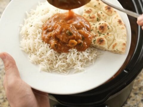 A slow cooker filled with creamy tikka masala chicken thighs, topped with a swirl of cashew cream and butter.