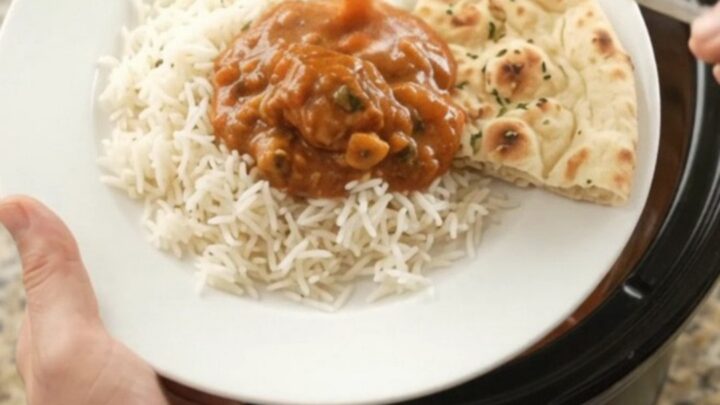 A slow cooker filled with creamy tikka masala chicken thighs, topped with a swirl of cashew cream and butter.
