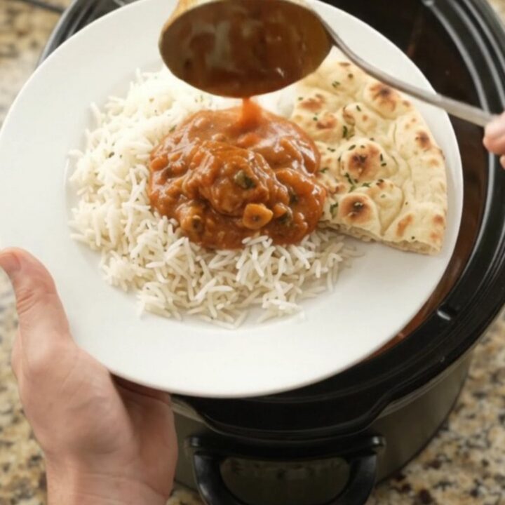 A slow cooker filled with creamy tikka masala chicken thighs, topped with a swirl of cashew cream and butter.
