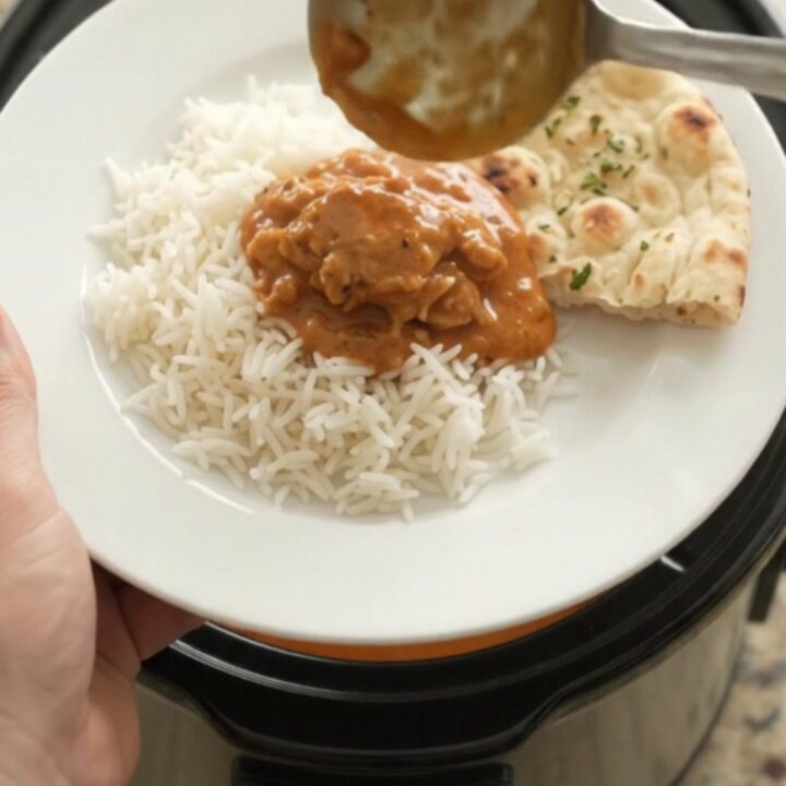 A slow cooker full of tender chicken thighs in a glossy orange-red makhani sauce with steam rising.